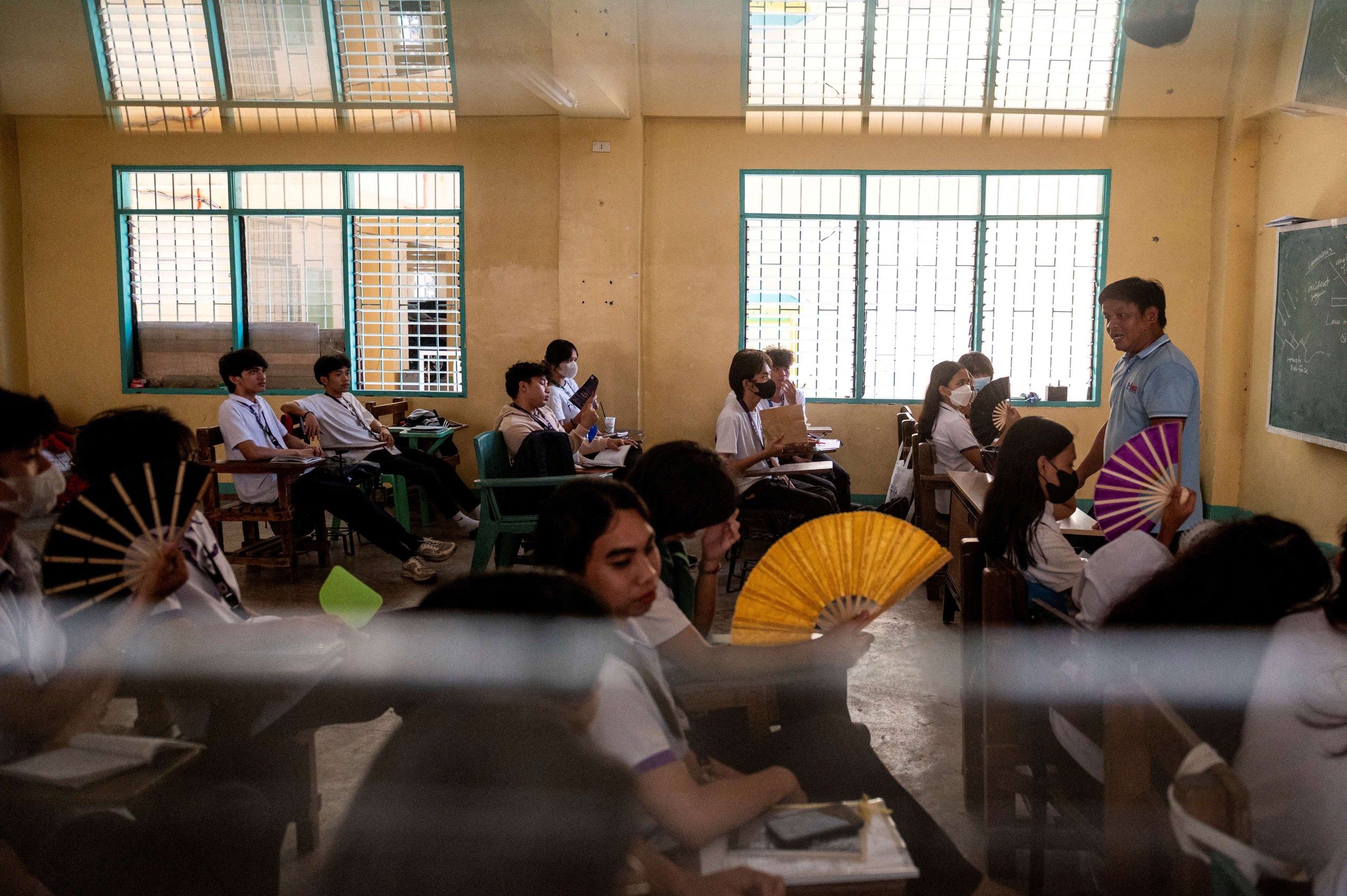 Học sinh lớp 12 dùng quạt tay, chịu đựng nắng nóng trong một lớp học tại Trường trung học Commonwealth, TP.Quezon, Philippines ngày 18.4